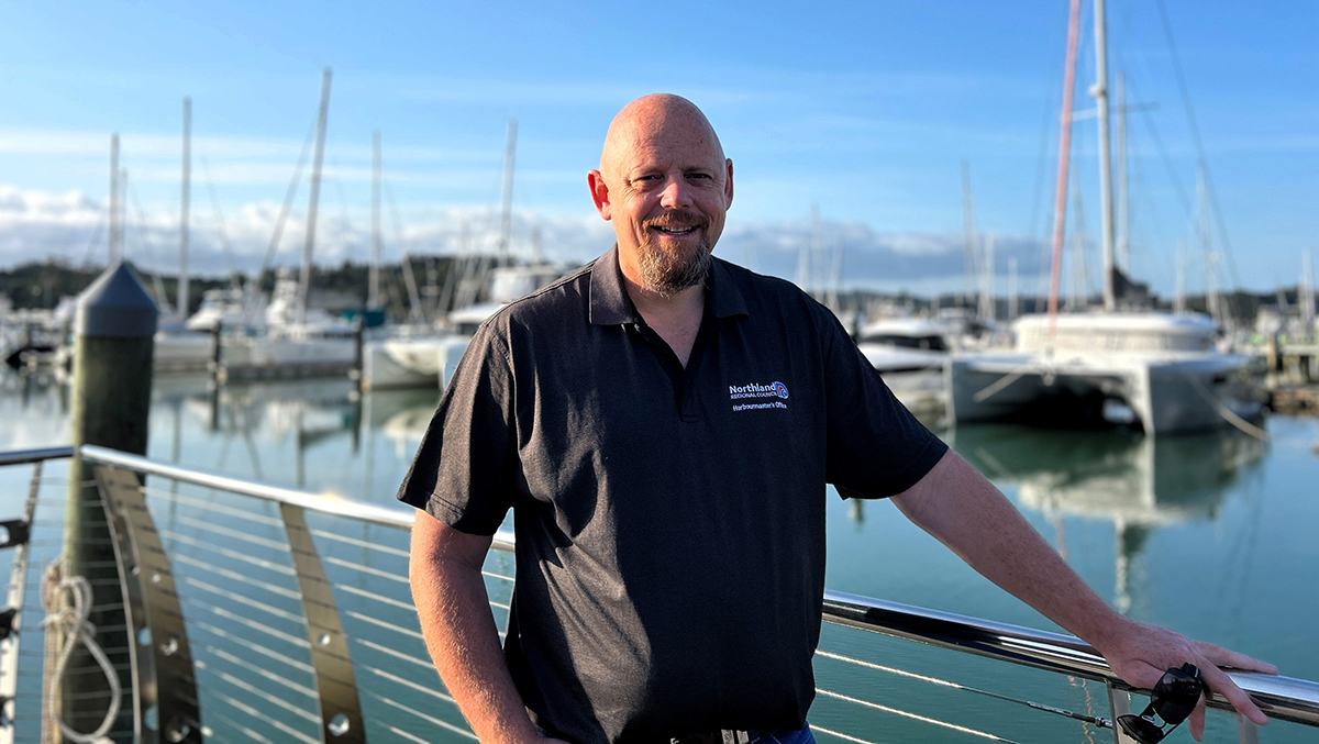 Man standing on a marina jetty with boats in the background.