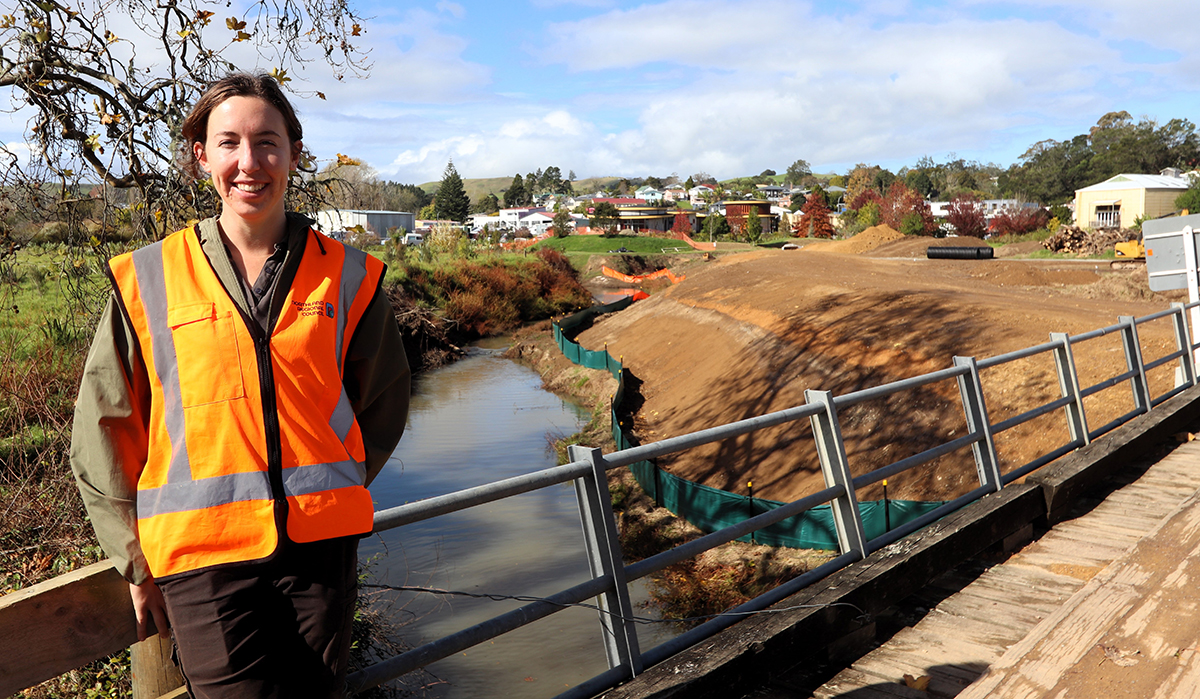 Woman wearing hi-vis vest on bridge with earthworks in the background.