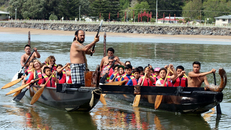 People paddling waka catamaran.