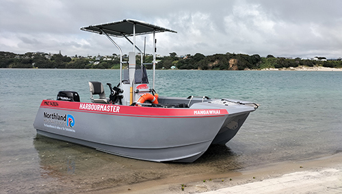 A small silver catamaran motor boat in shallow water near the beach.