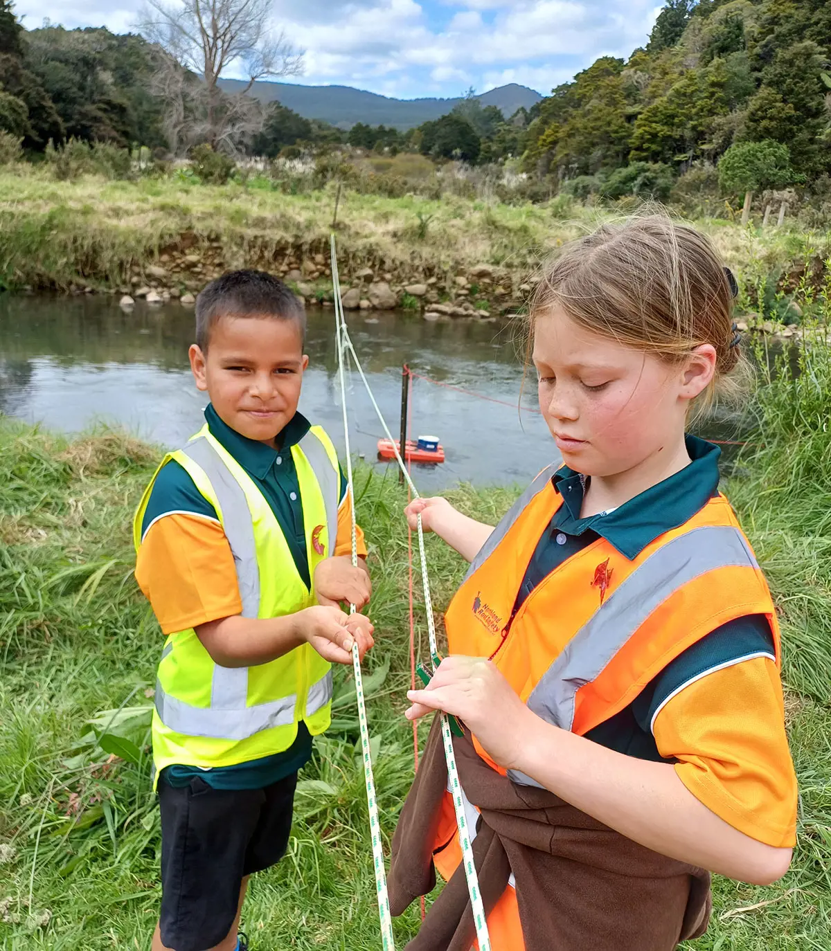 Two children with hydrology equipment by a river.