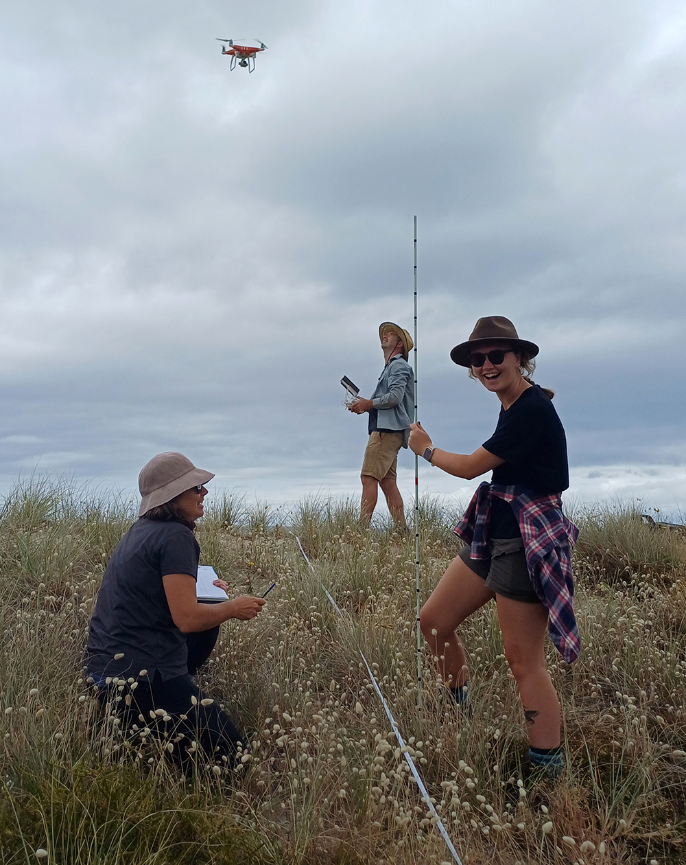 Three people on a sand dune using a drone.