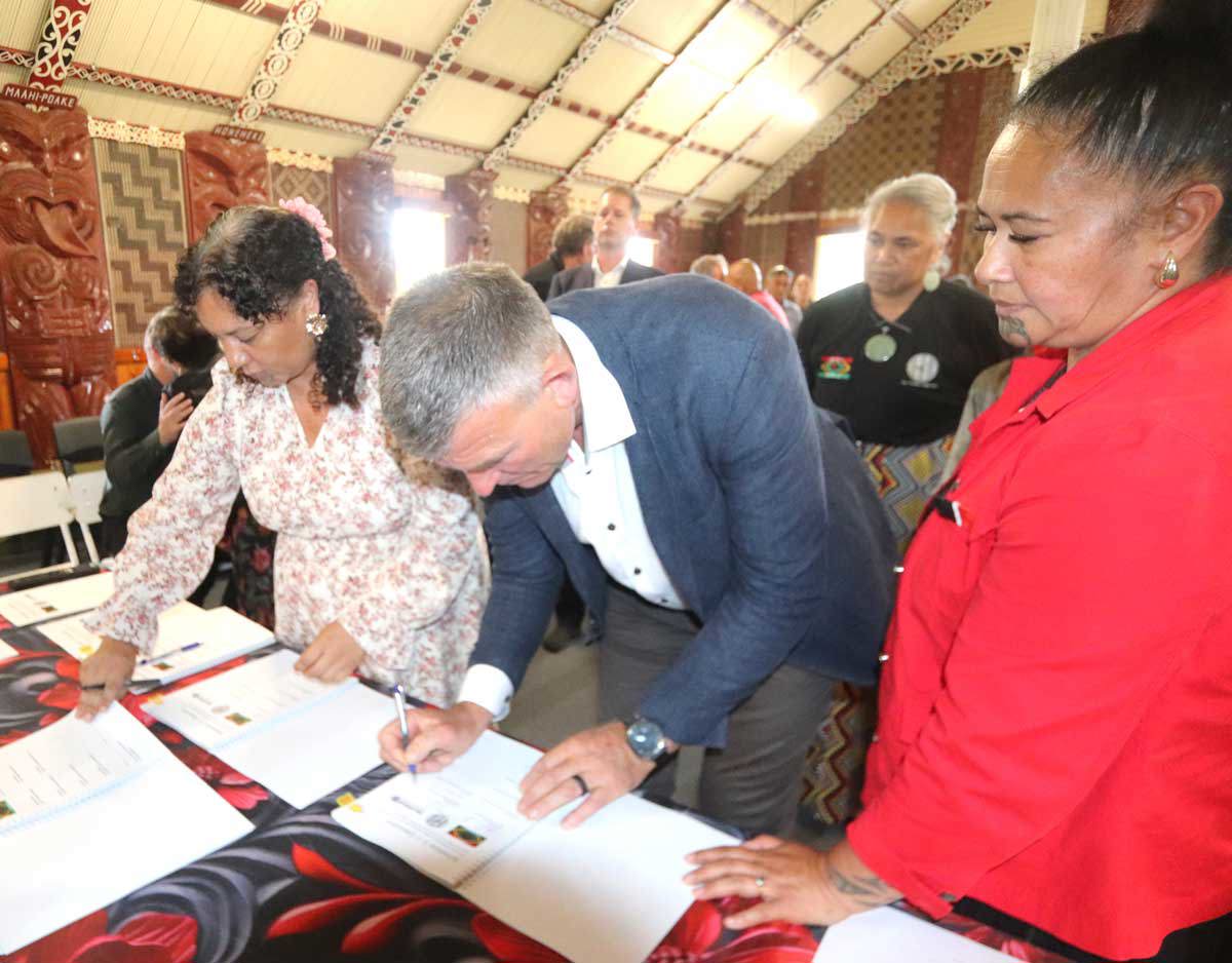 Two people signing documents with other people watching on.