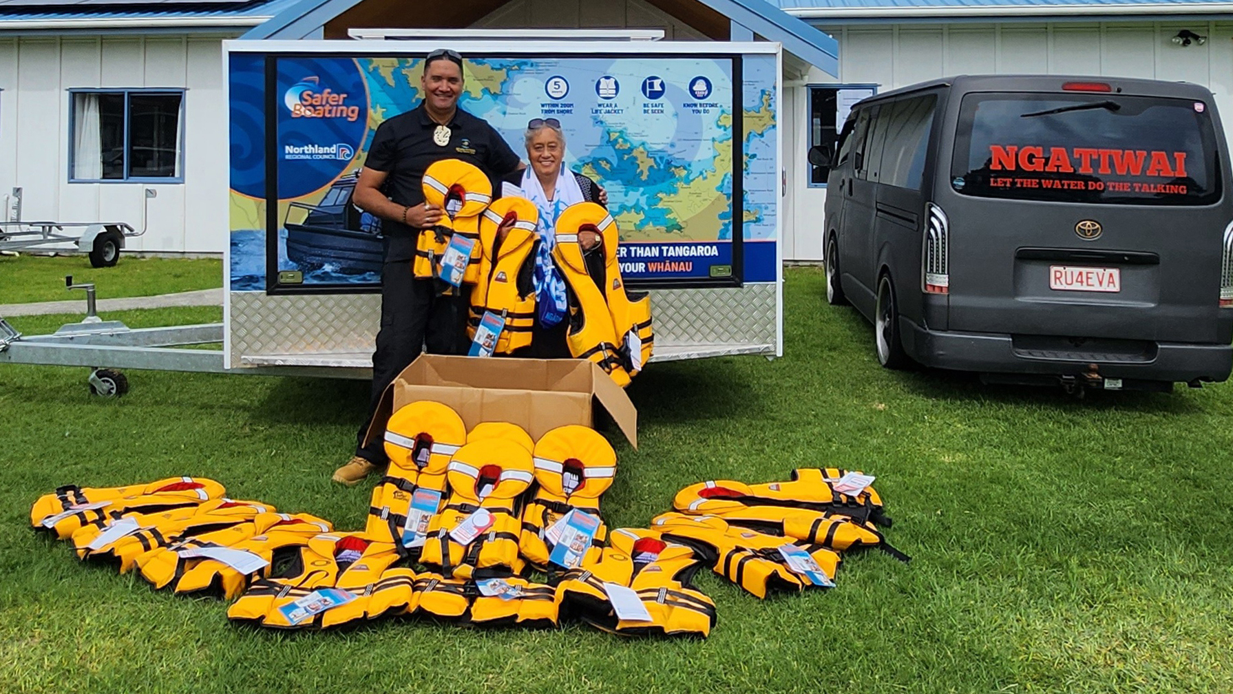 Two people with lifejackets in front of a trailer displaying a map.