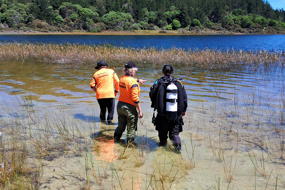 Two women in hi-vis and one in a wetsuit in the lake shallows.