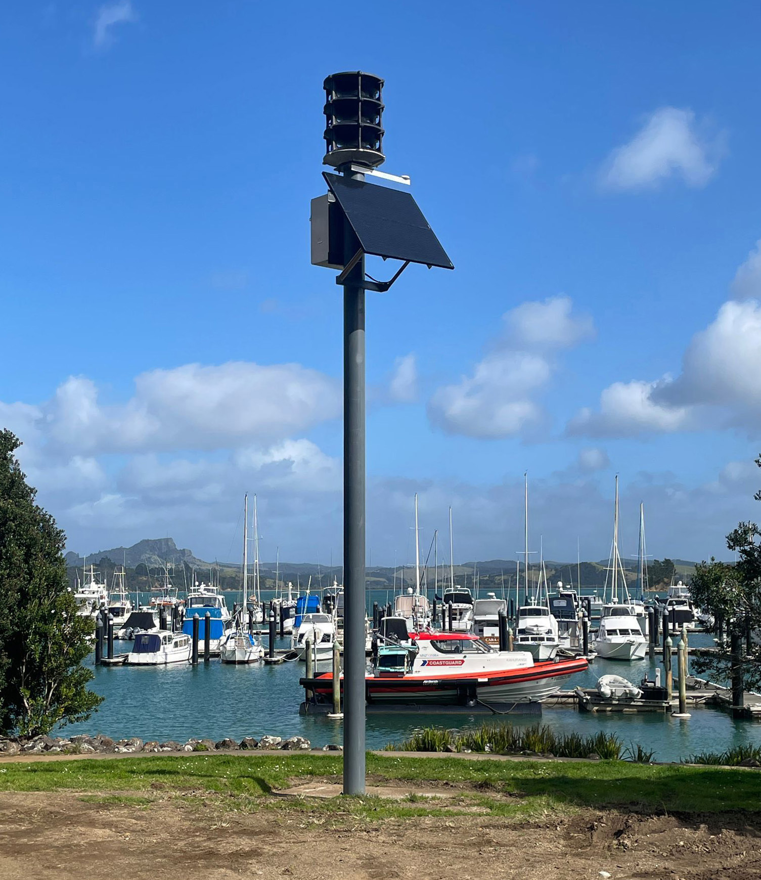 A tsunami siren pole near a marina with a coastguard boat and other boats in the background.