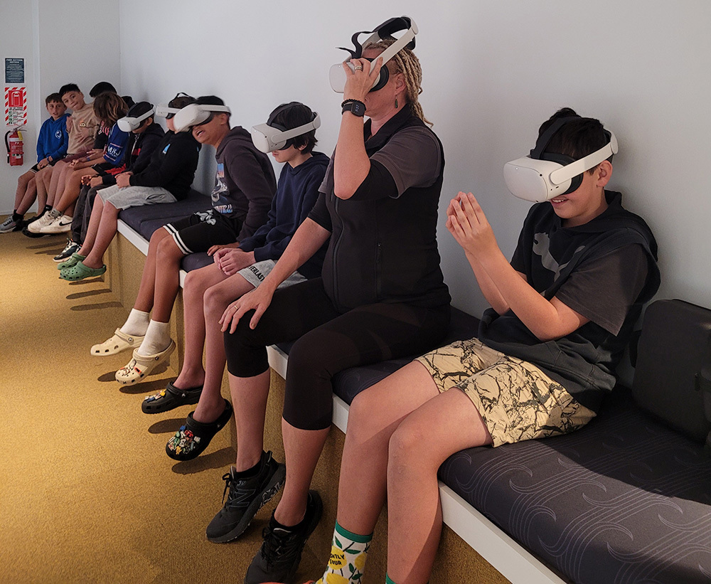 Students wearing VR headsets with others watching on.