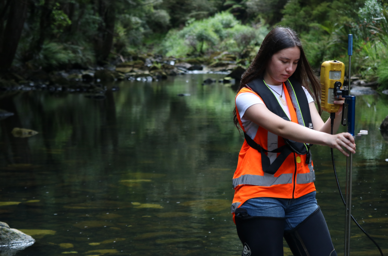 A girl standing in the river with a water monitoring tool.