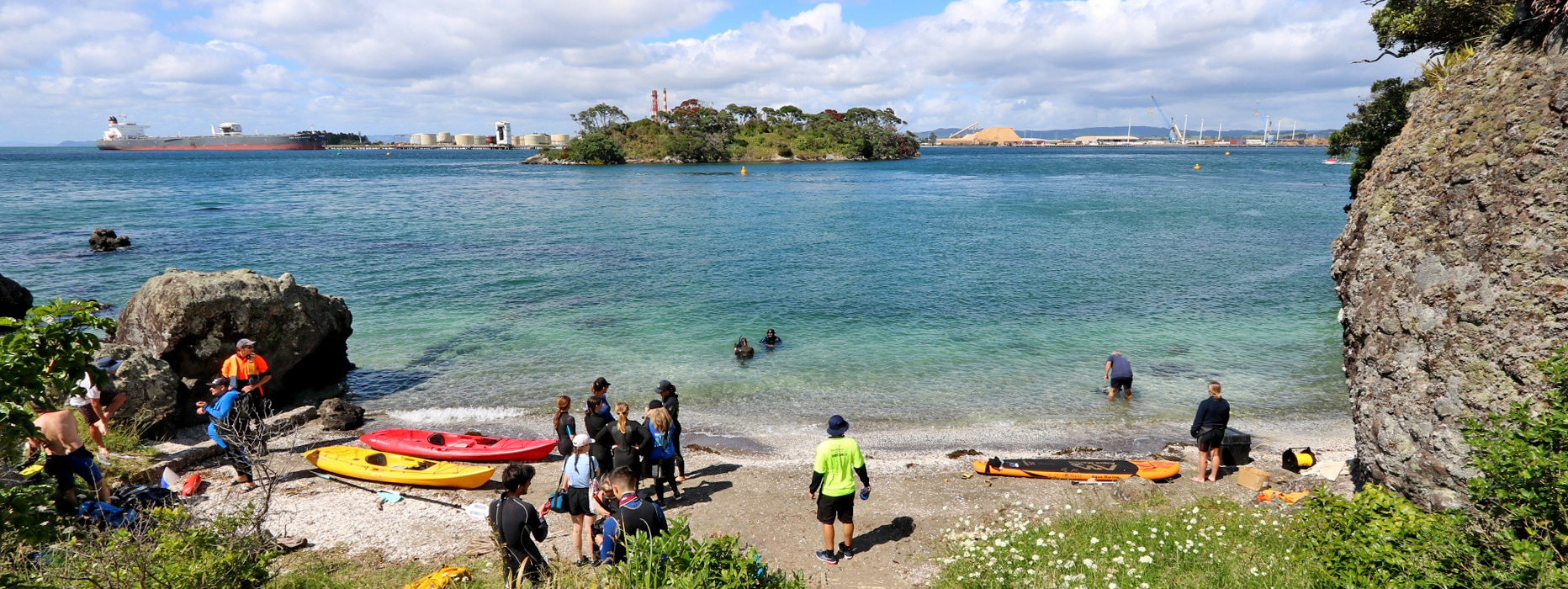 People on a beach in wetsuits with kayaks and snorkelling gear.