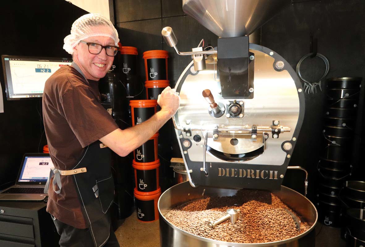 Man with coffee roasting machine, roasting coffee beans, wearing a hairnet and glasses